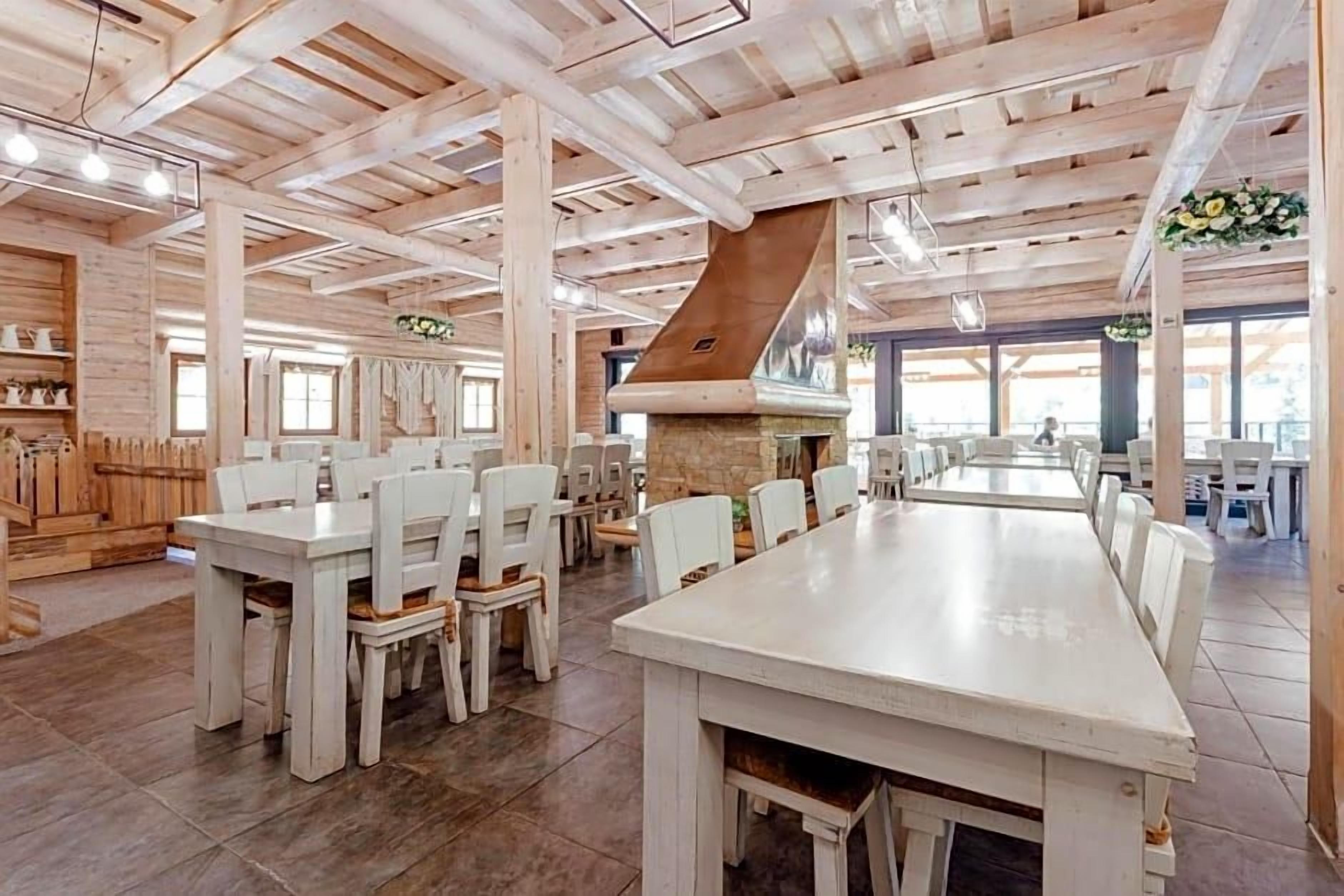 Un comedor amplio con mesas y sillas de madera, una chimenea de piedra y ventanas grandes que dejan entrar luz natural.