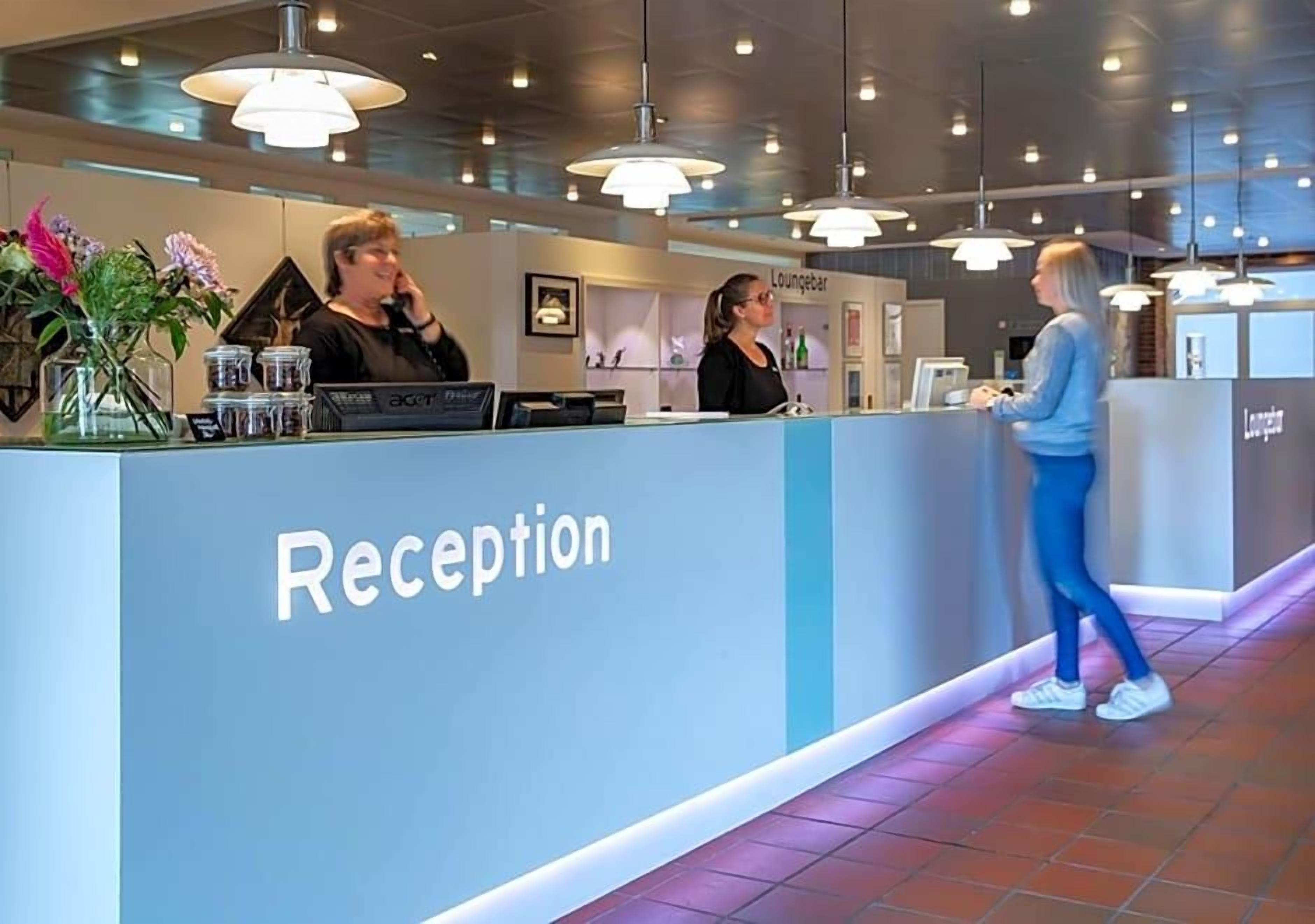A reception area with a counter, two staff members, and a lounge sign.