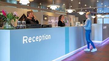 A reception area with a counter, two staff members, and a lounge sign.