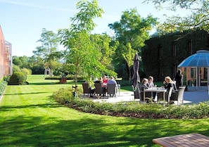 An outdoor seating area with tables and chairs, surrounded by greenery and a building in the background. - Pharmakon & Conferencecenter (Hillerod)