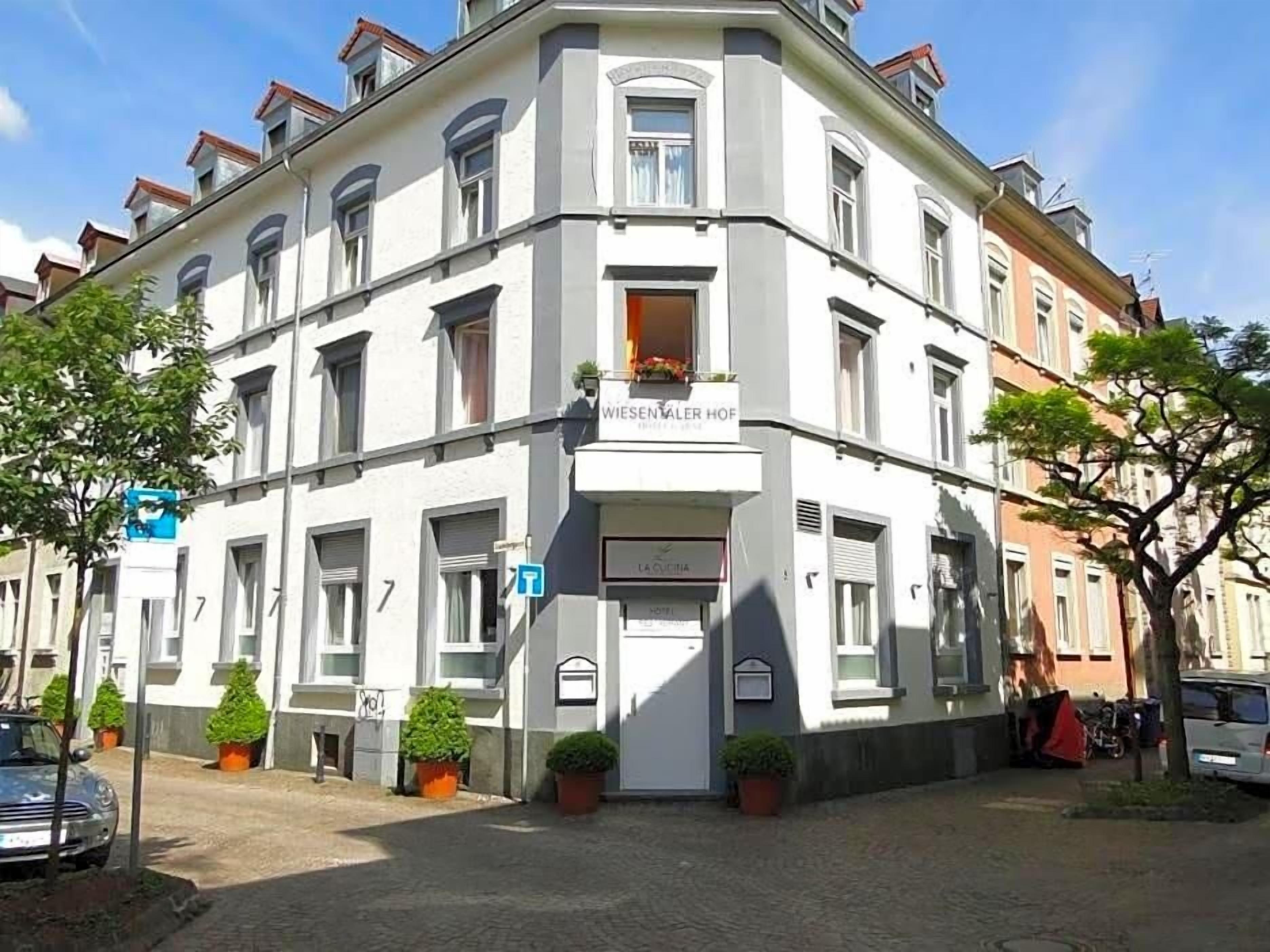 A corner building with a sign 'WIESENWALER HOF' and a 'LA CUVIERIA' sign.