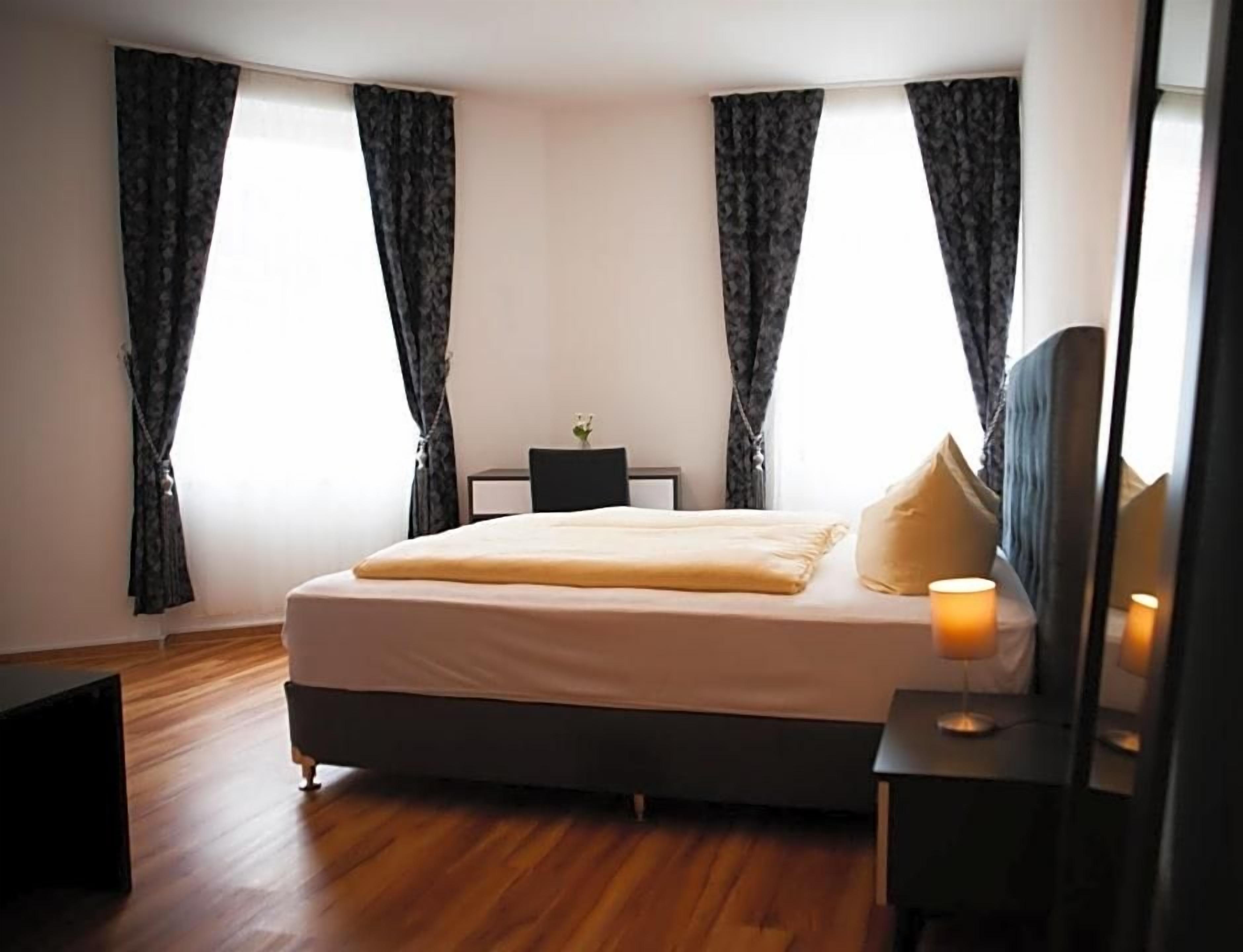 A bedroom with a bed, bedside table, lamp, and curtains.
