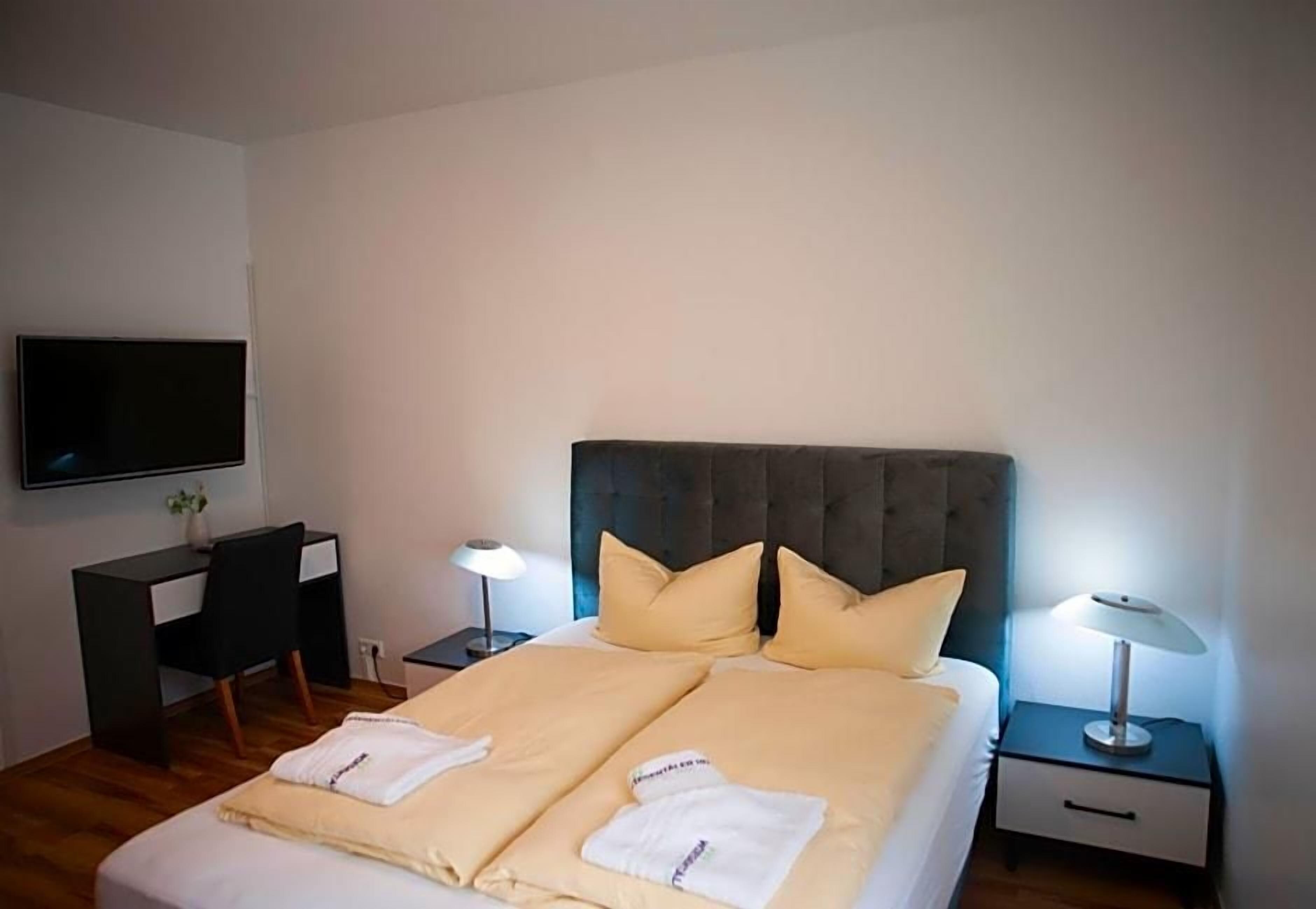 Een hotelkamer met een bed, nachtkastjes, een bureau, een stoel, een televisie en een lamp.
