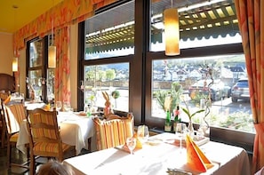 Un restaurante con mesas preparadas para comer, amplios ventanales con vistas al exterior y lámparas colgantes.