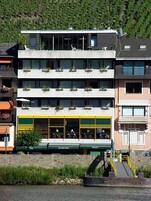 Un hotel de varios pisos con balcones, un restaurante con terraza y vistas al río.