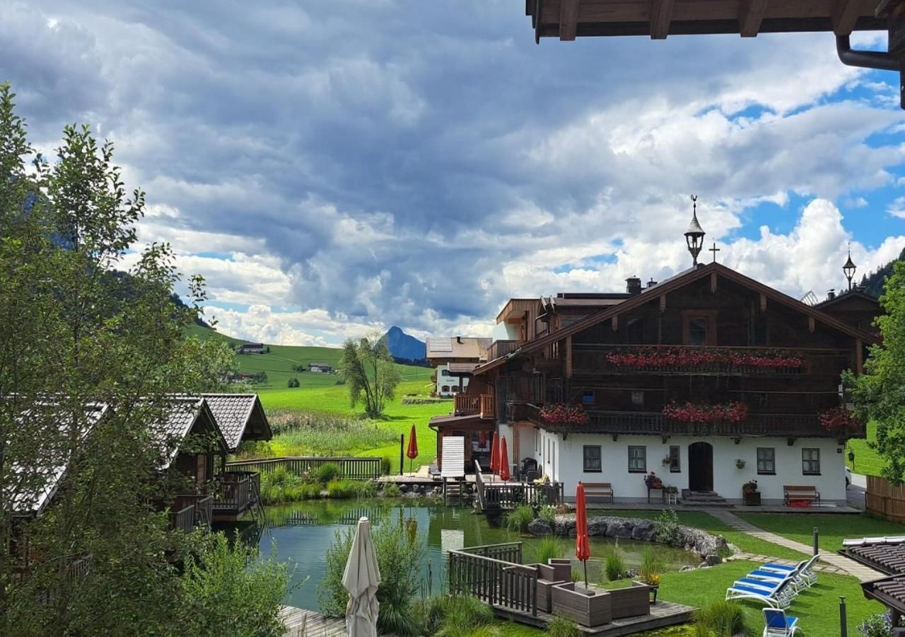 En traditionell alpchata med en damm, omgiven av frodig grönska och en klar himmel.