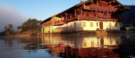 Un edificio de madera con balcón, ubicado junto a un cuerpo de agua tranquilo.