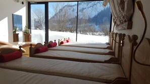 Ein Hotelzimmer mit vier Betten an einer Wand, einem großen Fenster mit Blick auf eine verschneite Landschaft und einem hölzernen Kopfteil.