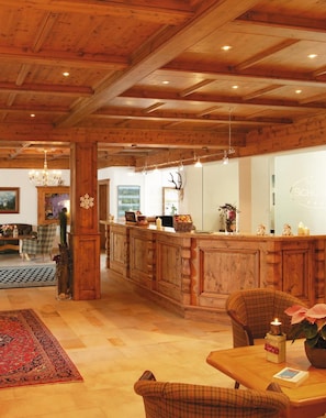 Ein Holzinneres mit einer Rezeption, einer Chandelüster und einem Essbereich mit Teppich und Tisch.