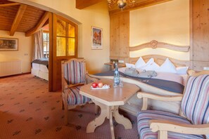 Um quarto acolhedor com teto de madeira, cama com travesseiros brancos, poltronas estofadas listradas e uma mesa com maçãs e garrafas.