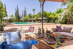 A poolside dining area with outdoor furniture, a pool, and lush greenery. - A Private Palace Escape — Marrakech-Safi 1000 (Marrakech-Safi)