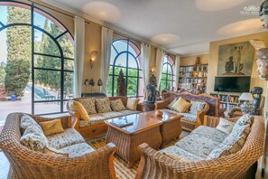 A spacious living room with wicker furniture, large windows, and a bookshelf. - A Private Palace Escape — Marrakech-Safi 1000 (Marrakech-Safi)