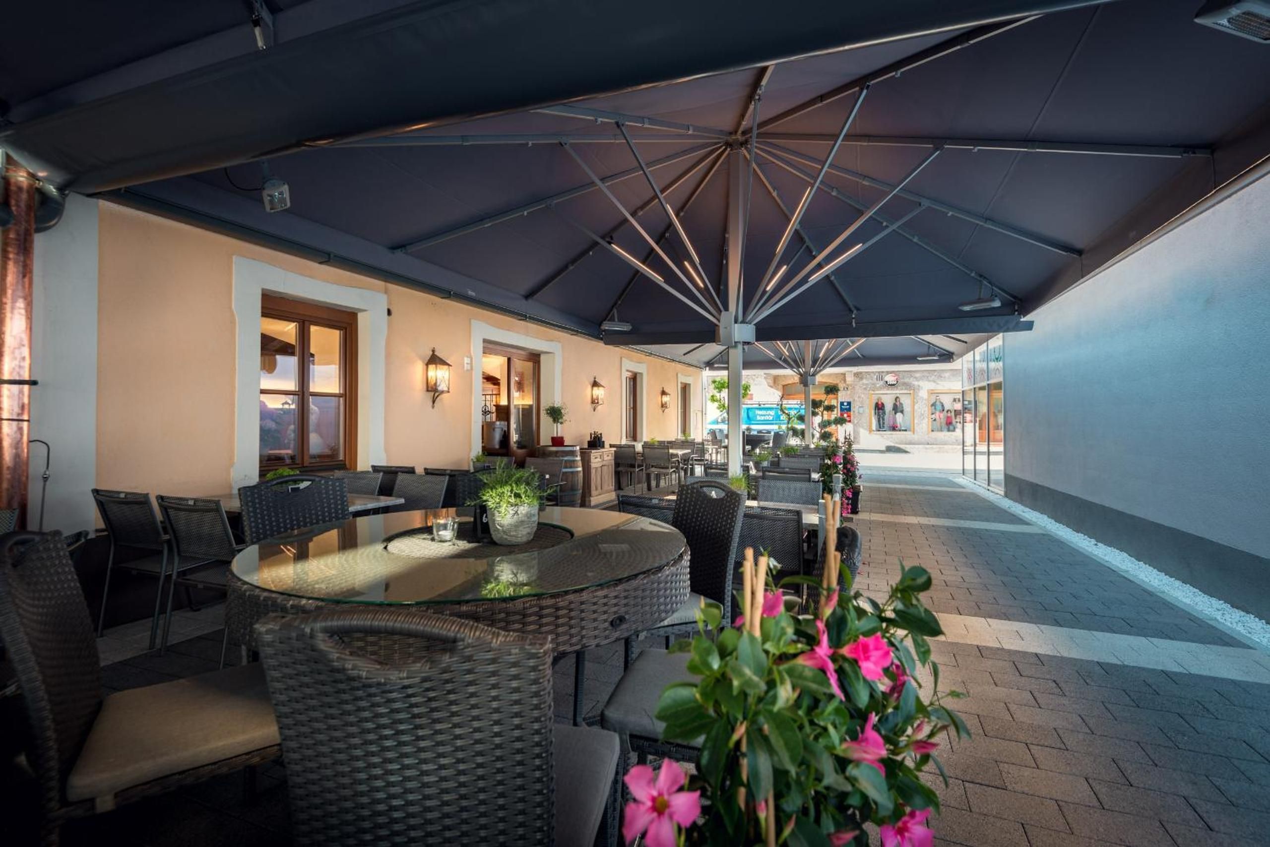 An outdoor seating area with round tables and chairs, a large umbrella, and a view of the street.