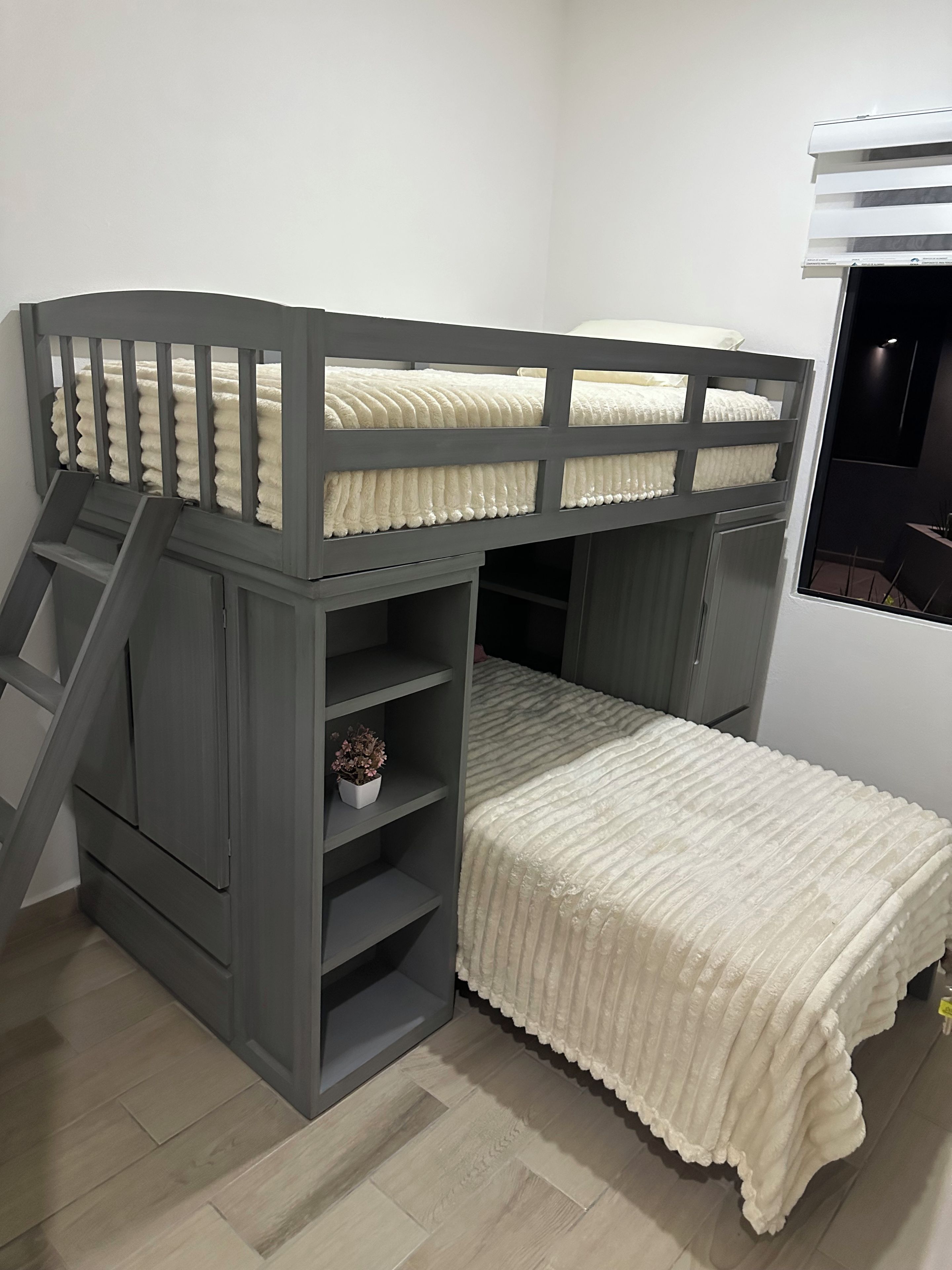 A bunk bed with a ladder, a small shelf with a plant, and a window with blinds.