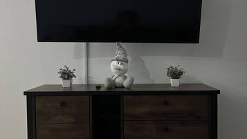 A flat-screen TV mounted on a wall above a dark wooden cabinet with two potted plants and a decorative item.
