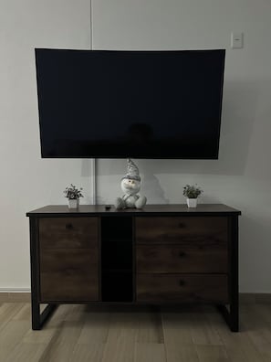 A flat-screen TV mounted on a wall above a dark wooden cabinet with two potted plants and a decorative item. - Beautiful apartment 5 minutes from GNP Stadium and Palacio Dep. (Ciudad de México)