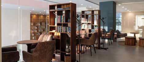 A modern library with bookshelves, comfortable seating, and a glass wall.