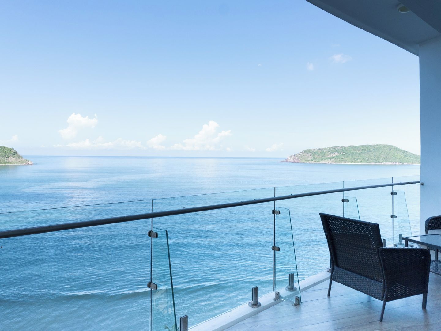 Ein Balkon mit Glasgeländer mit Blick auf ein ruhiges Meer und das entfernte Land.