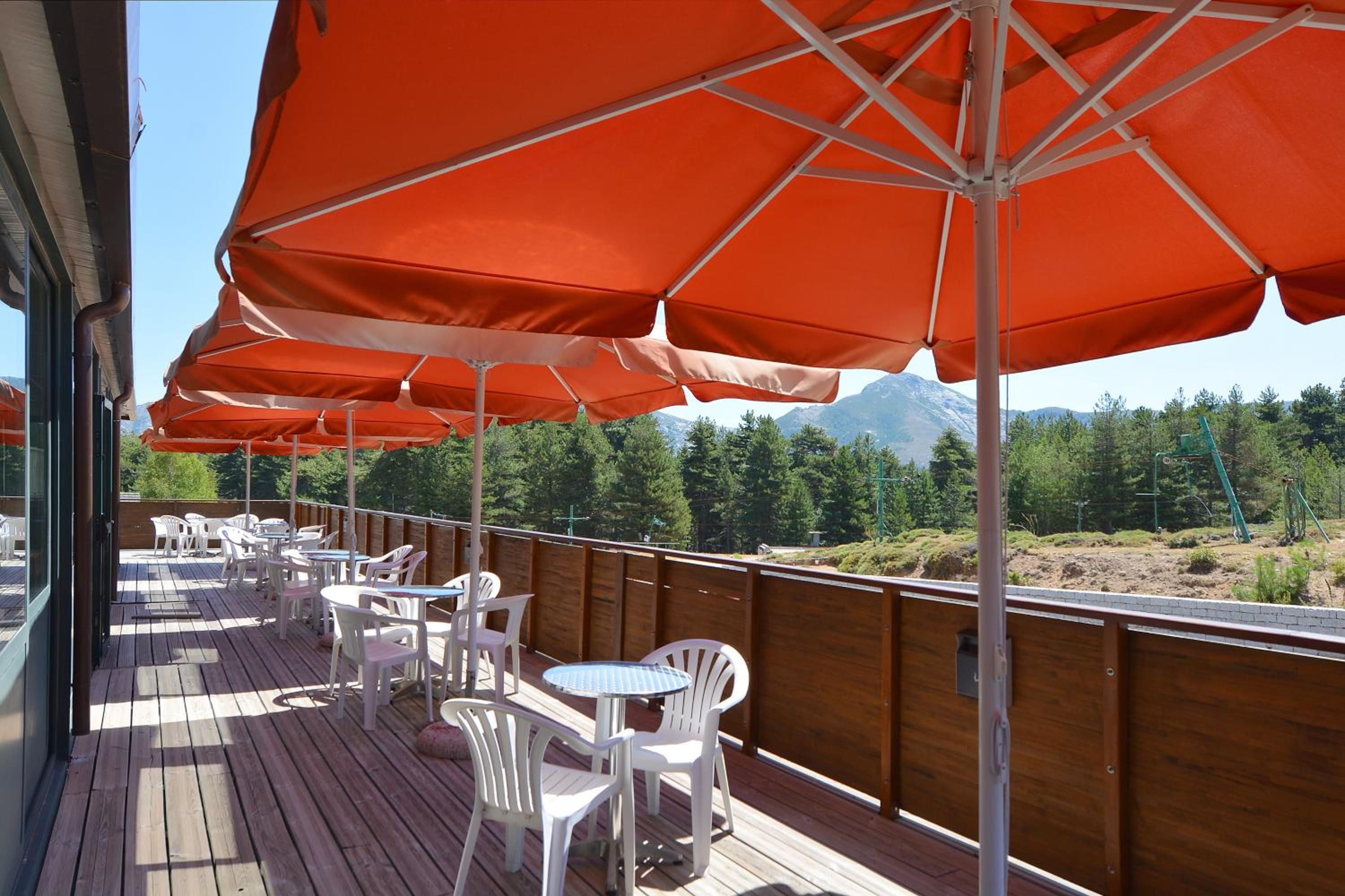 A deck with outdoor seating and umbrellas, overlooking a mountainous landscape.