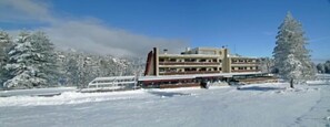 Un hotel de varios pisos con techo plano y una torre central, rodeado de árboles cubiertos de nieve.