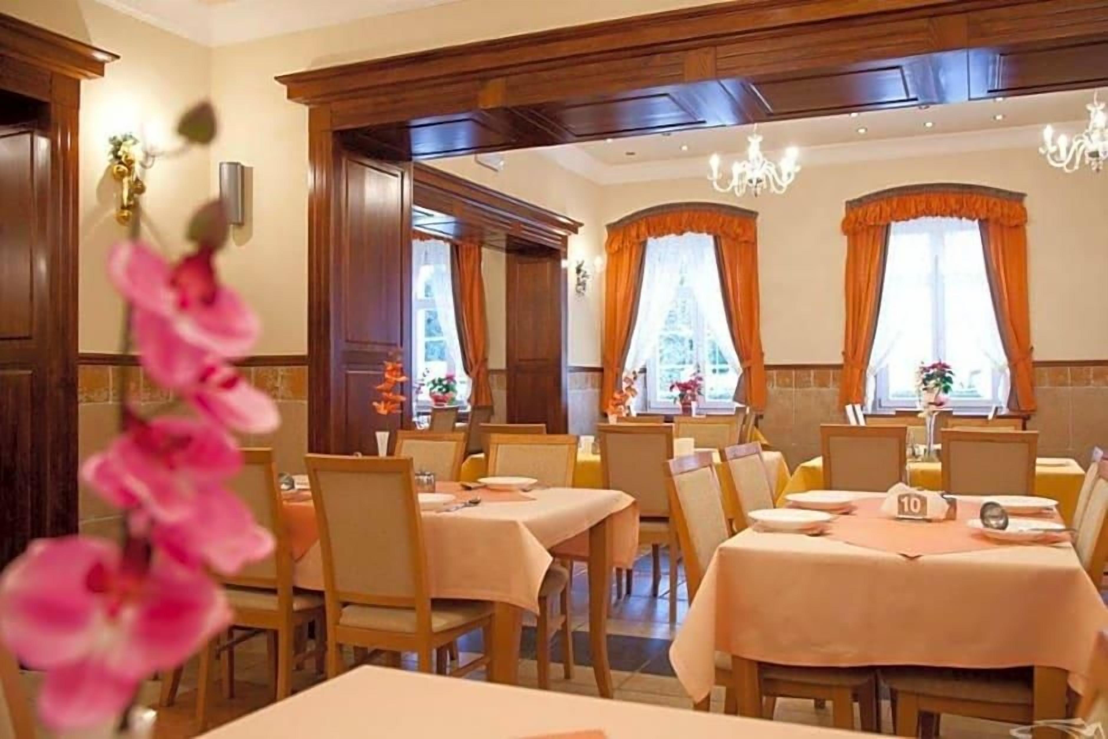 A dining area with tables set for service, wooden paneling on the walls, and a chandelier.