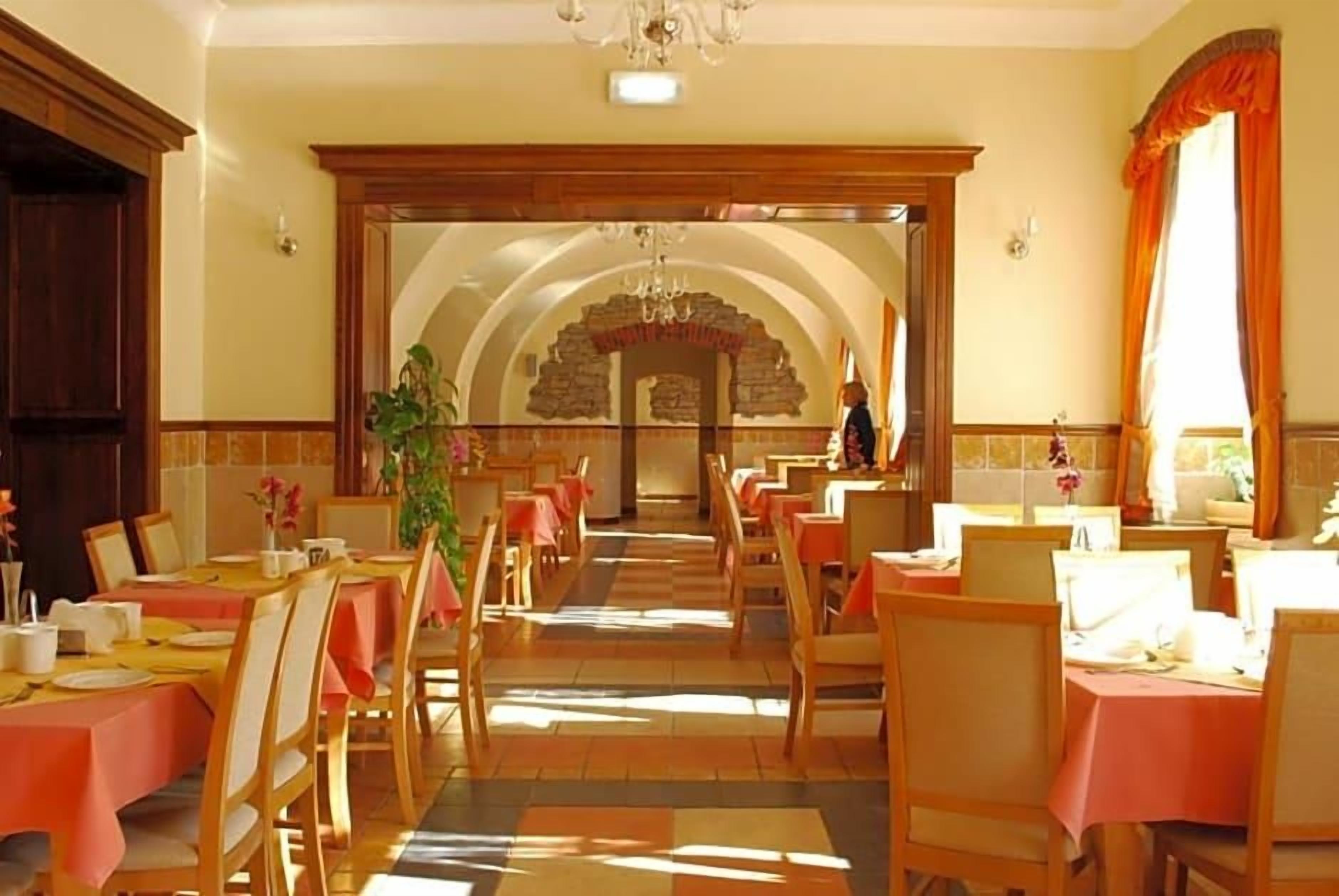 A dining area with tables set for service, a chandelier, and a brick archway leading to another room.