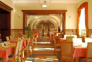Un comedor con mesas dispuestas para el servicio, una araña y un arco de ladrillo que conduce a otra estancia.