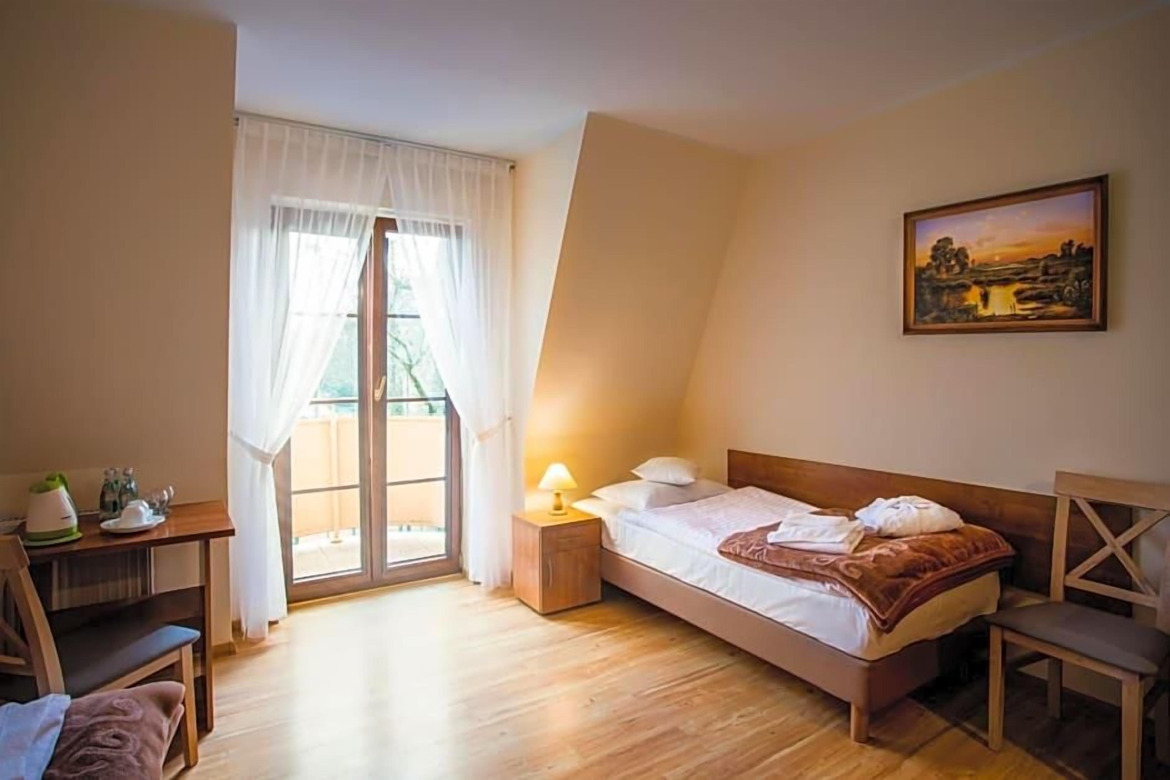 A bedroom with a bed, a desk, a chair, a lamp, and a painting on the wall.