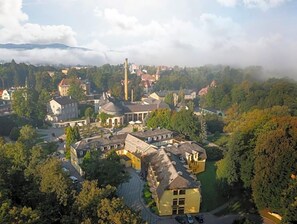 Un complejo histórico de edificios con varias estructuras, incluyendo una torre destacada, rodeado de vegetación exuberante y un paisaje montañoso.