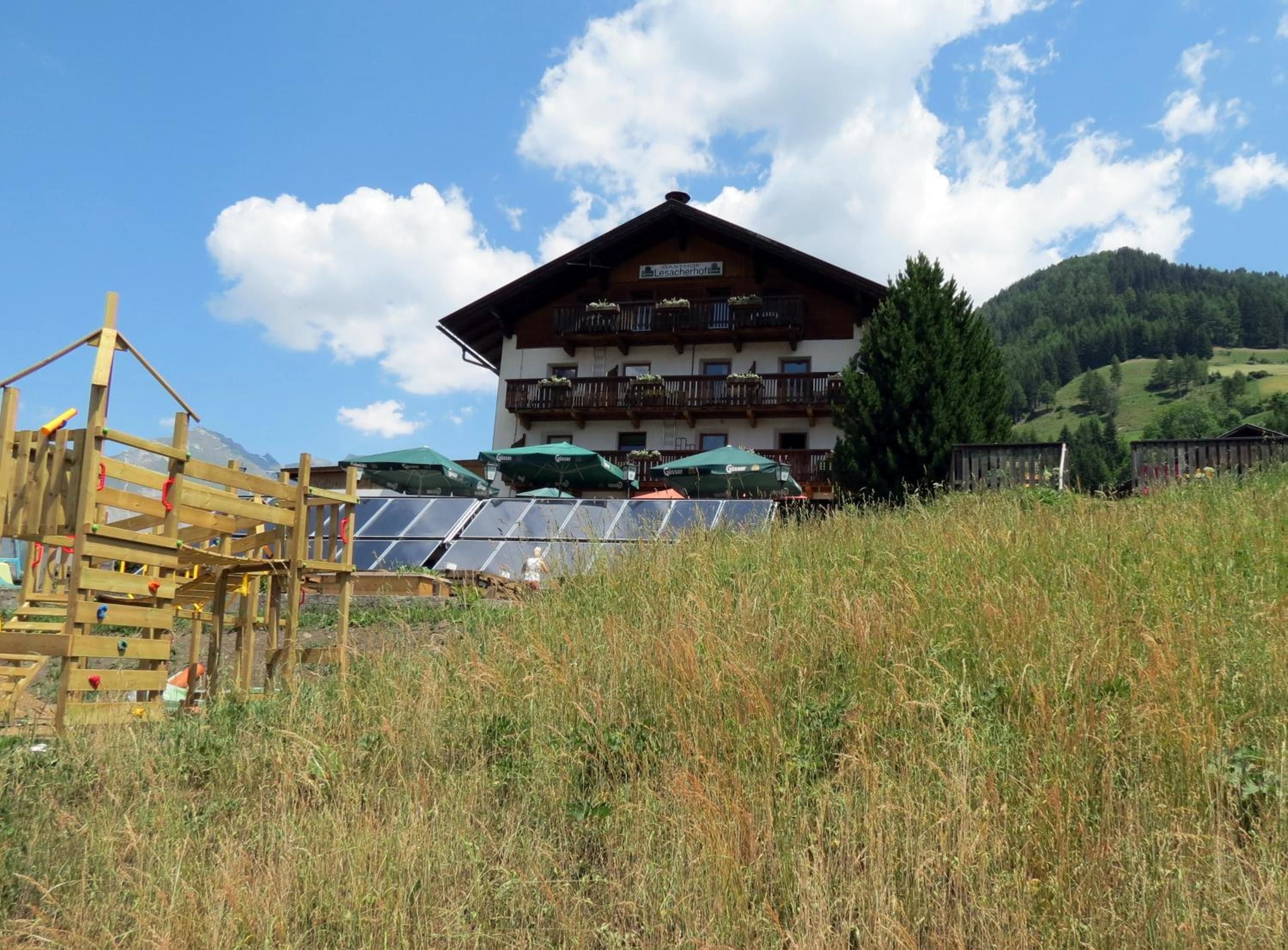 A wooden chalet with a balcony, solar panels, and a mountain backdrop.