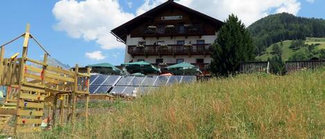A wooden chalet with a balcony, solar panels, and a mountain backdrop.
