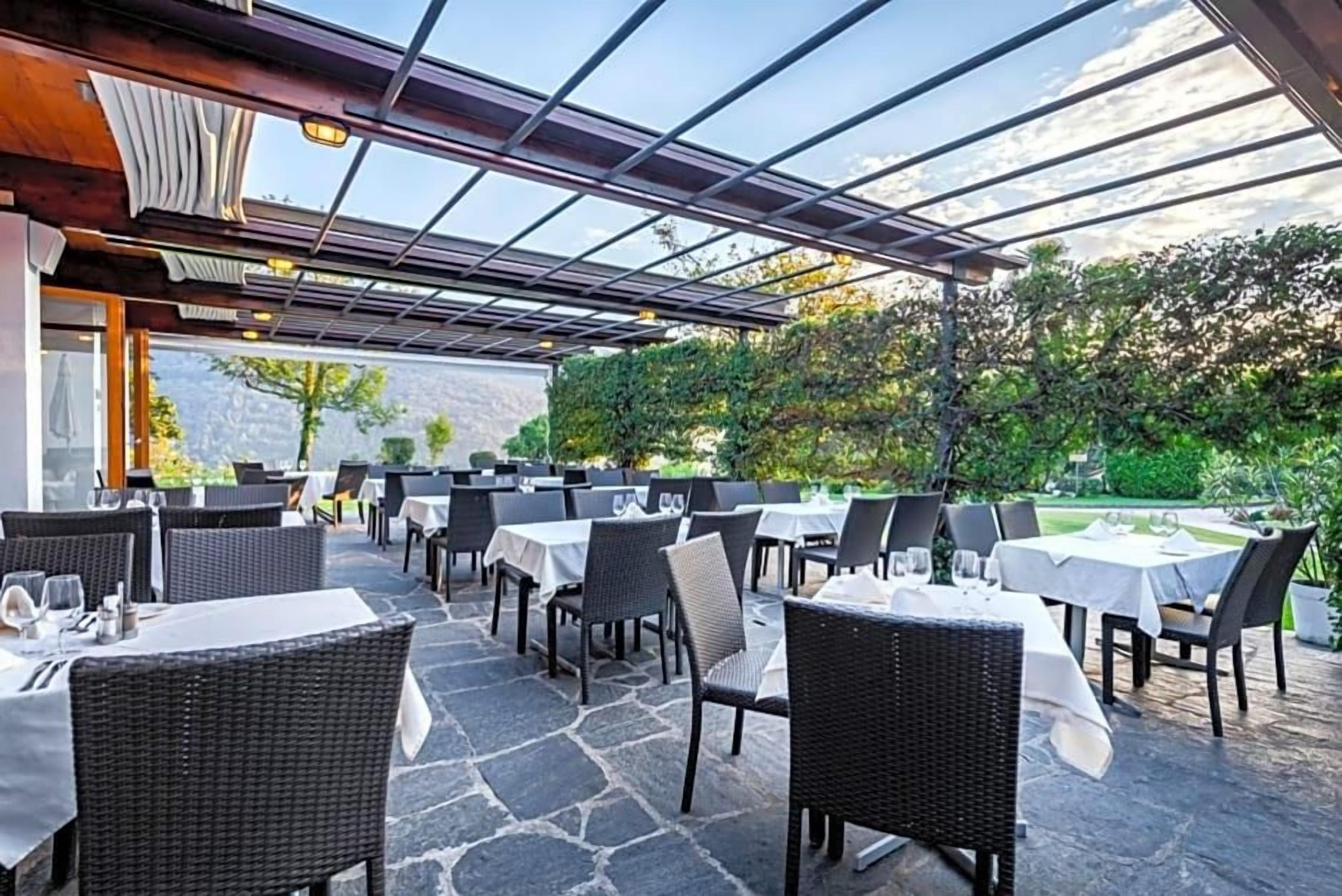 Un área de comedor al aire libre con mesas y sillas, un pérgola y vistas a la vegetación.