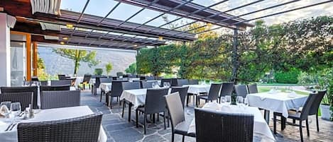 Un área de comedor al aire libre con mesas y sillas, un pérgola y vistas a la vegetación.