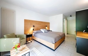 Ein modernes Hotelzimmer mit einem Bett, Nachttischen, einem Schreibtisch und einem Sessel.