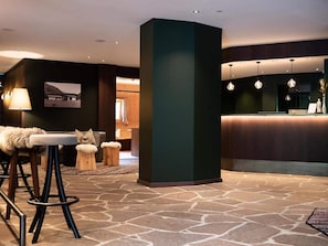 A reception area with a stone floor, a reception desk, and a bar area with stools. - Anabel (Valle Aurina)