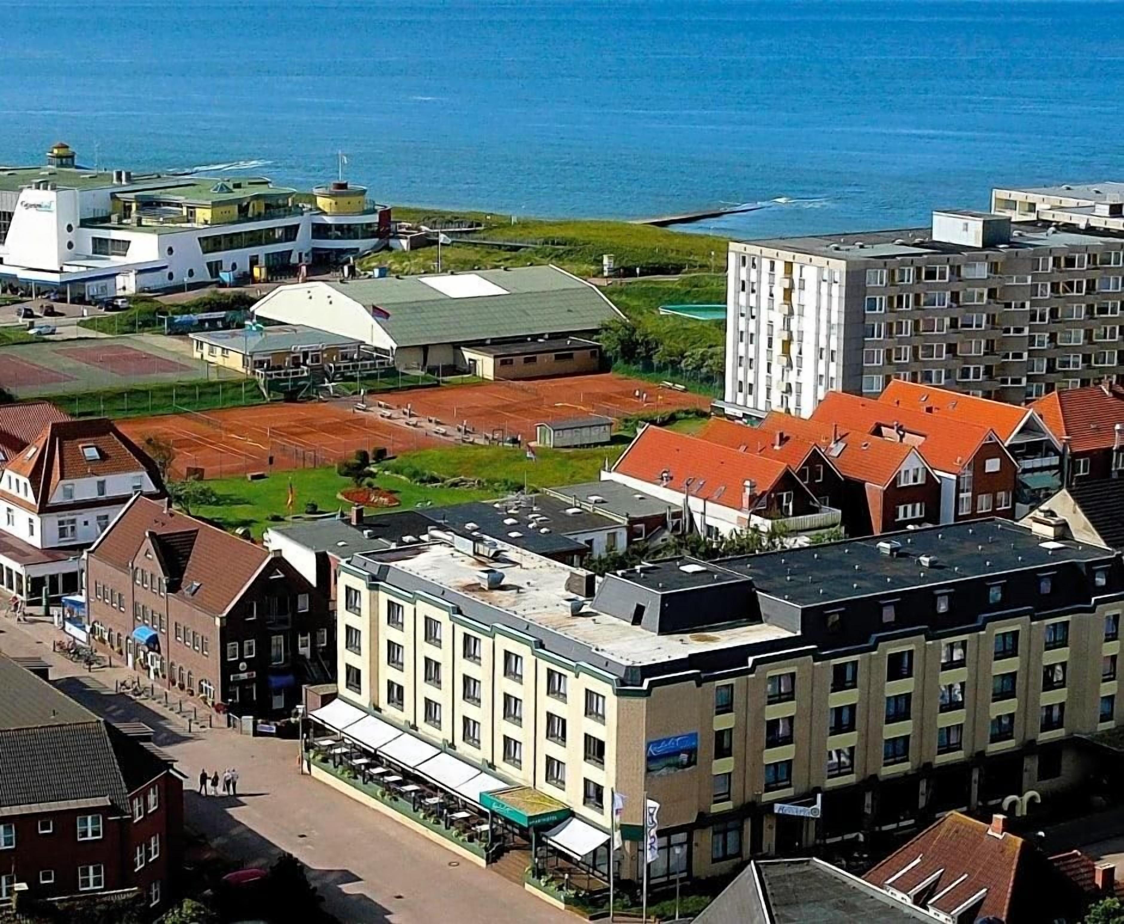 A coastal hotel with multiple buildings, a parking area, and a view of the sea.