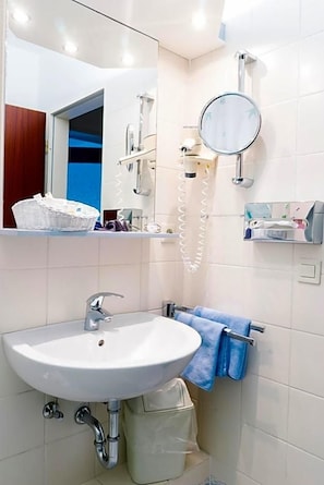 A bathroom with a white sink, a mirror, a towel rack, and a shower area. - Aparthotel Kachelot (Borkum)