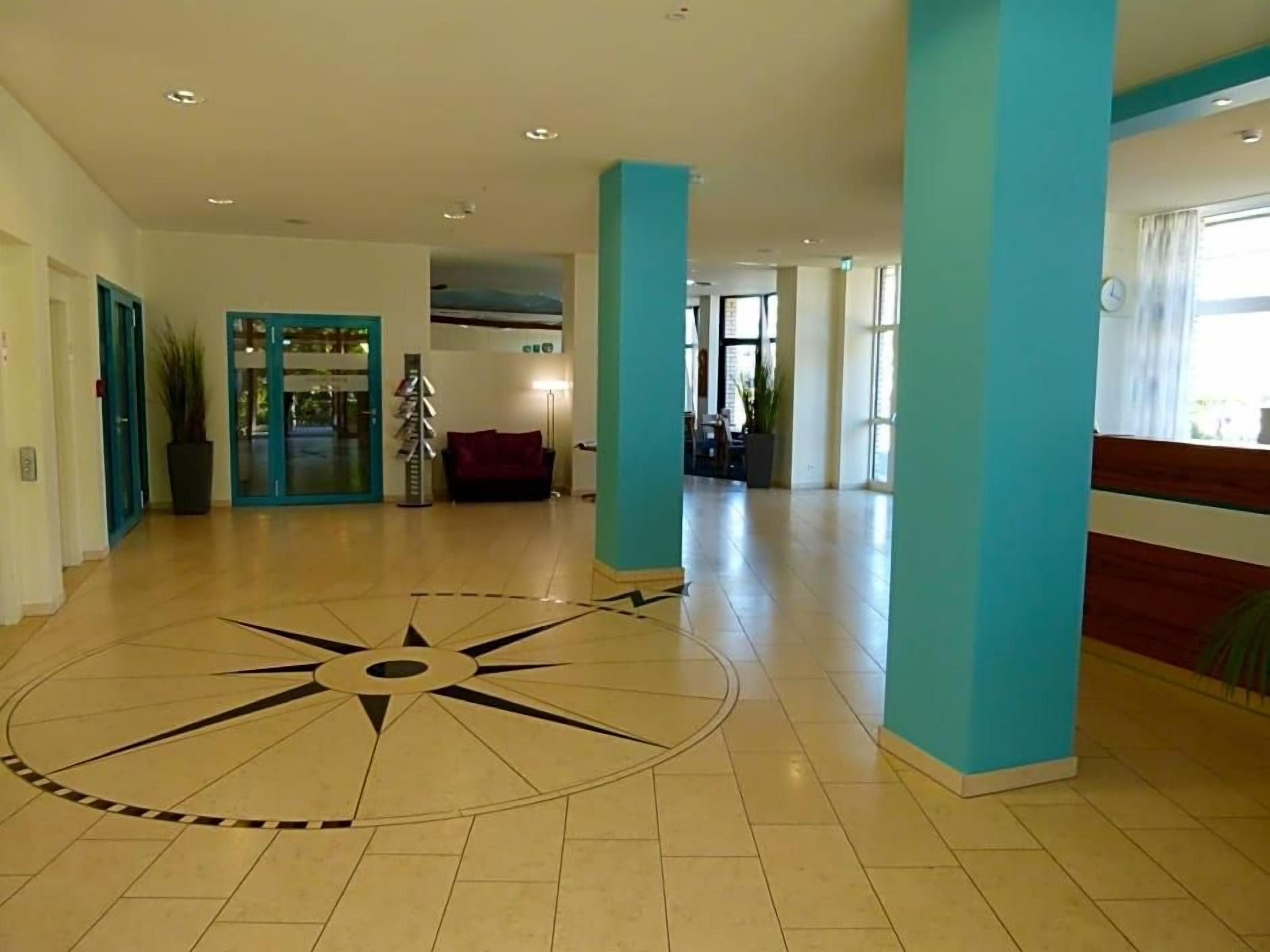 Eine großzügige Lobby mit großflächigem Bodenmuster, einer Rezeption und einer Sitzecke.