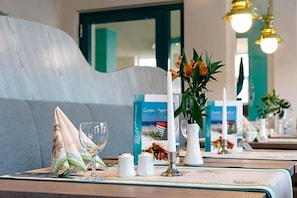 A dining table with a menu, a candle, and a vase with flowers. - Aparthotel Kachelot (Borkum)