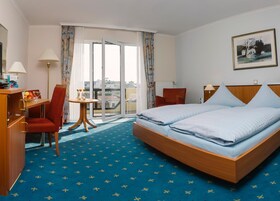 A hotel room with a bed, a desk, a chair, a small table, and a view of the city through the window.