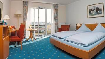Ein Hotelzimmer mit Bett, Schreibtisch, Stuhl, kleinem Tisch und Blick auf die Stadt durch das Fenster.