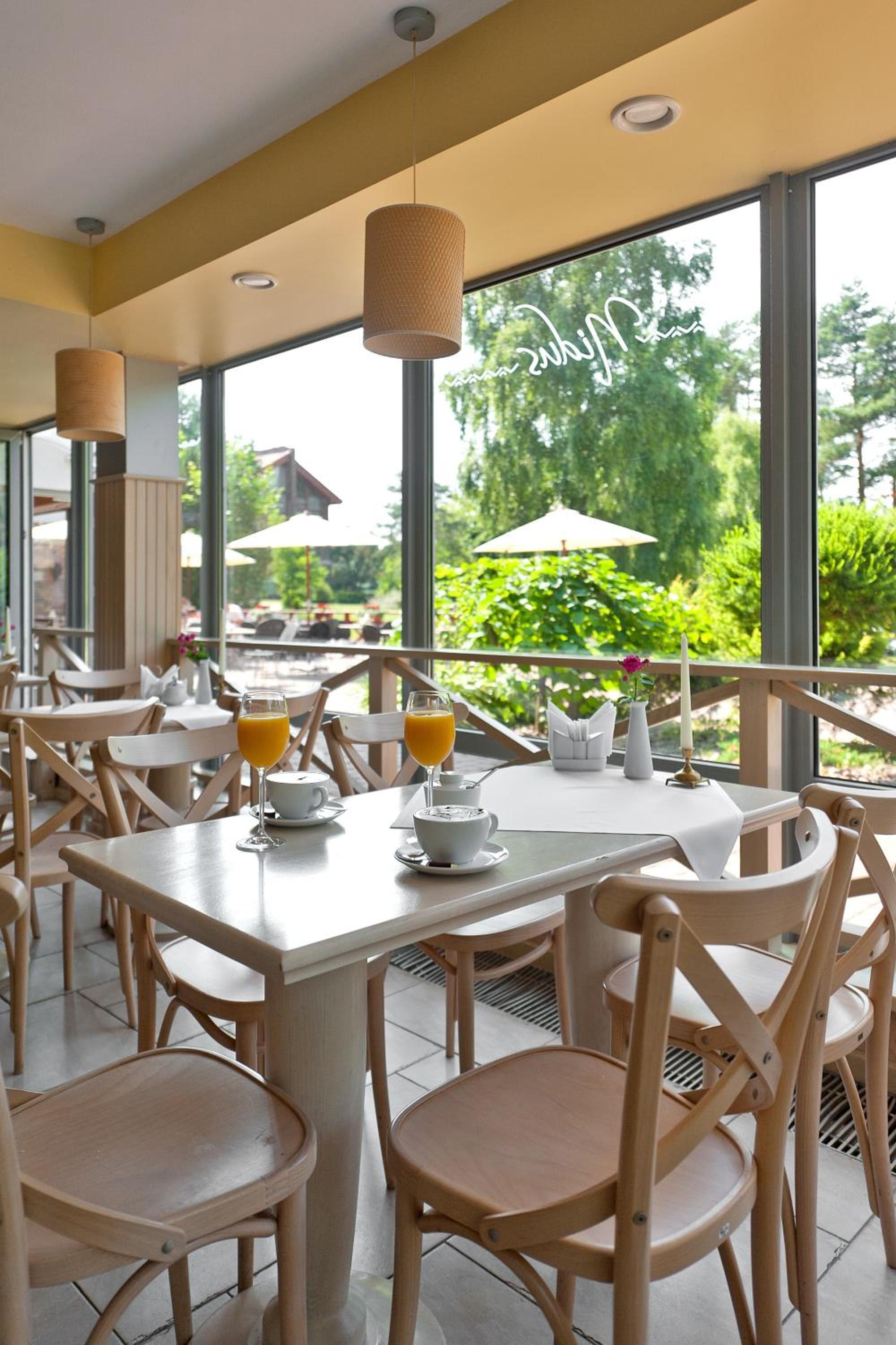 A restaurant with outdoor seating, tables with chairs, and a view of greenery.