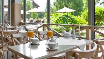 A restaurant with outdoor seating, tables with chairs, and a view of greenery.