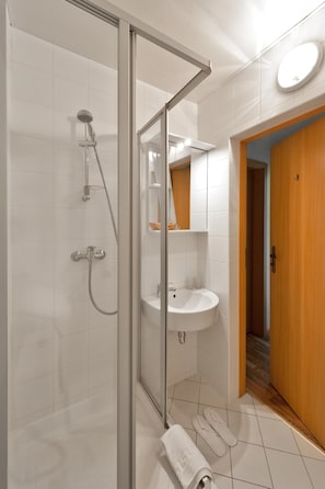 Un baño moderno con ducha de vidrio, lavamanos blanco y puerta de madera.