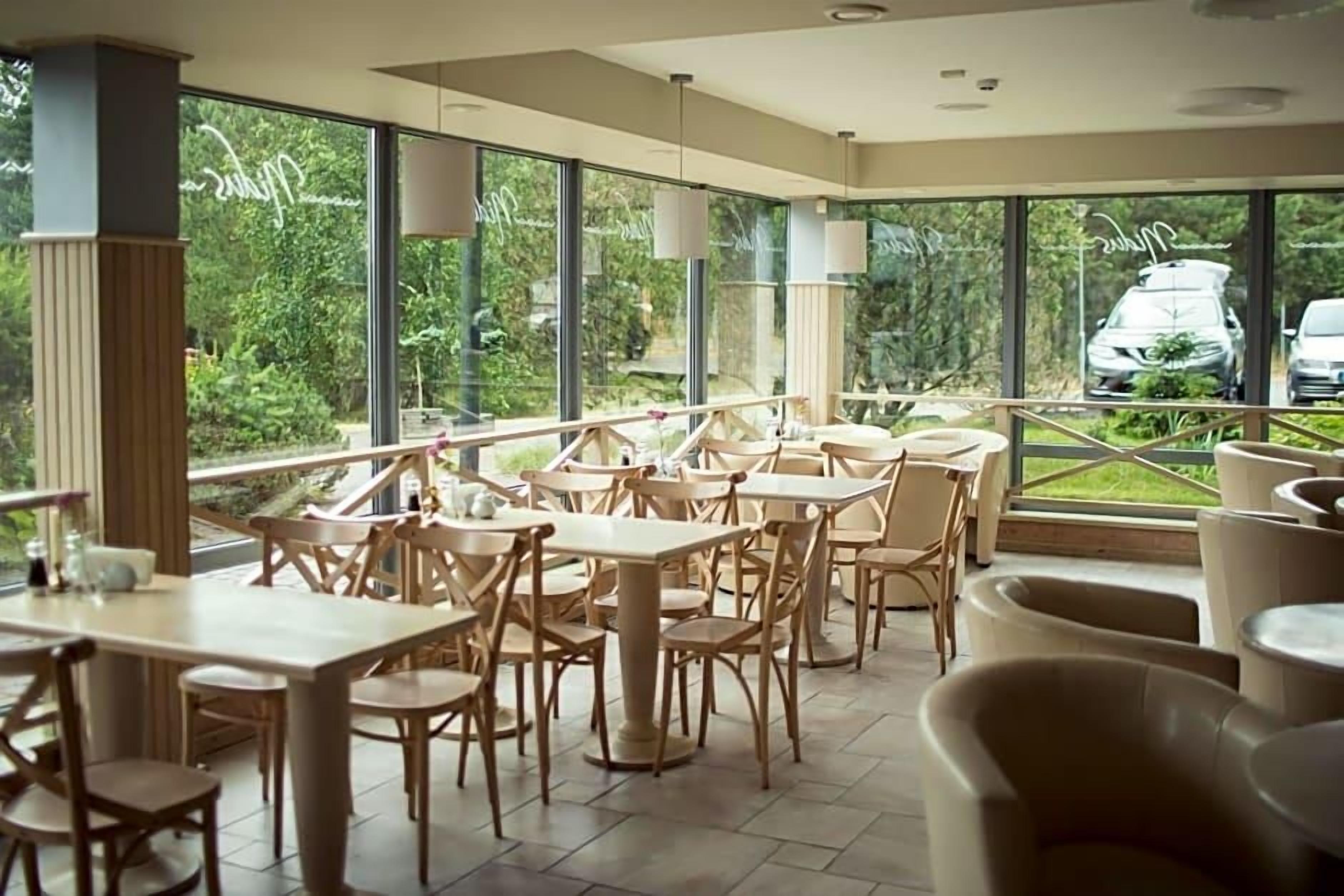 A restaurant with outdoor seating, large windows, and a view of greenery.