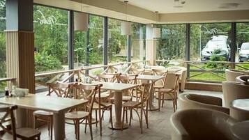A restaurant with outdoor seating, large windows, and a view of greenery.