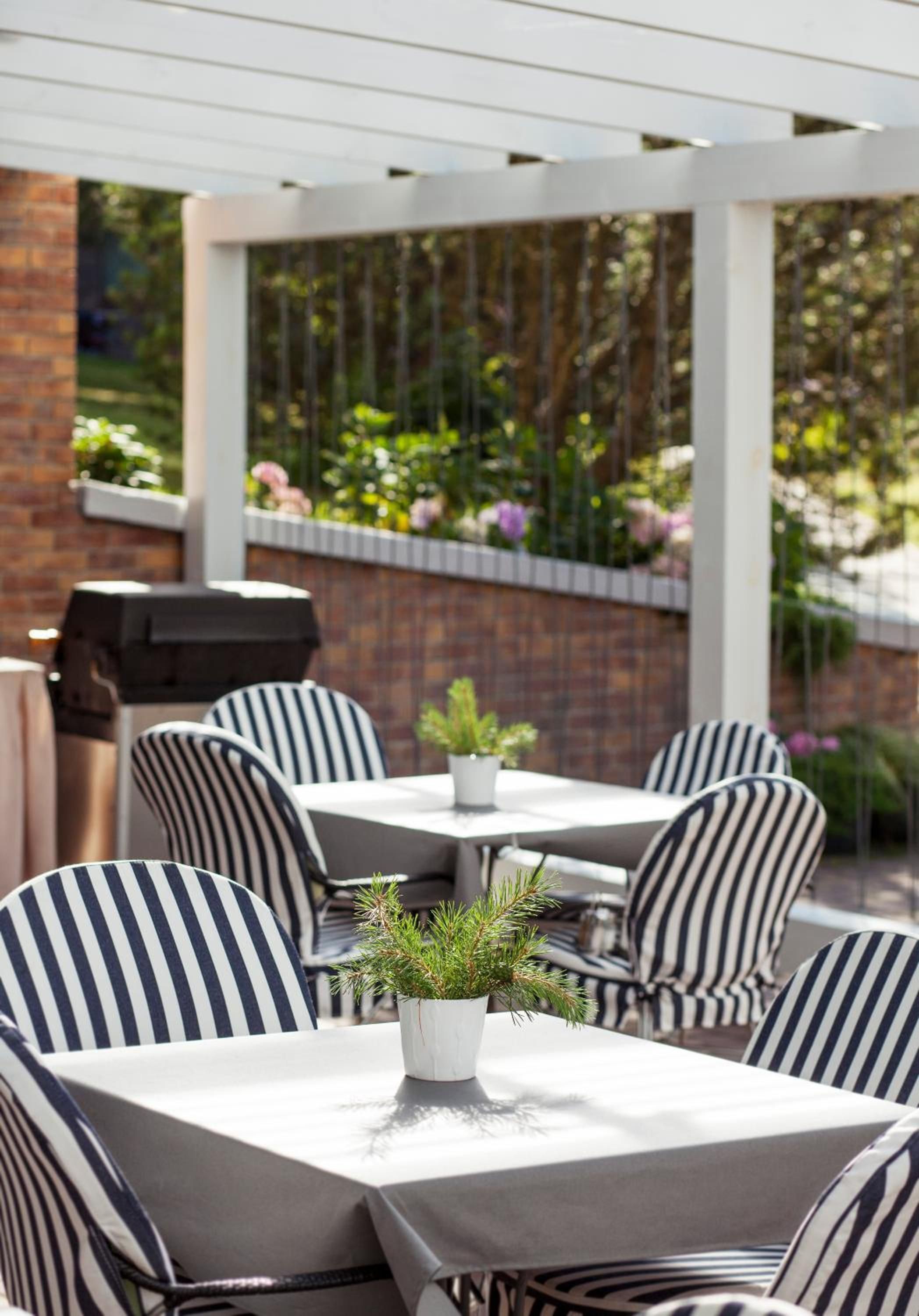 Un patio al aire libre con sillas y mesas a rayas, una parrilla y plantas en macetas.