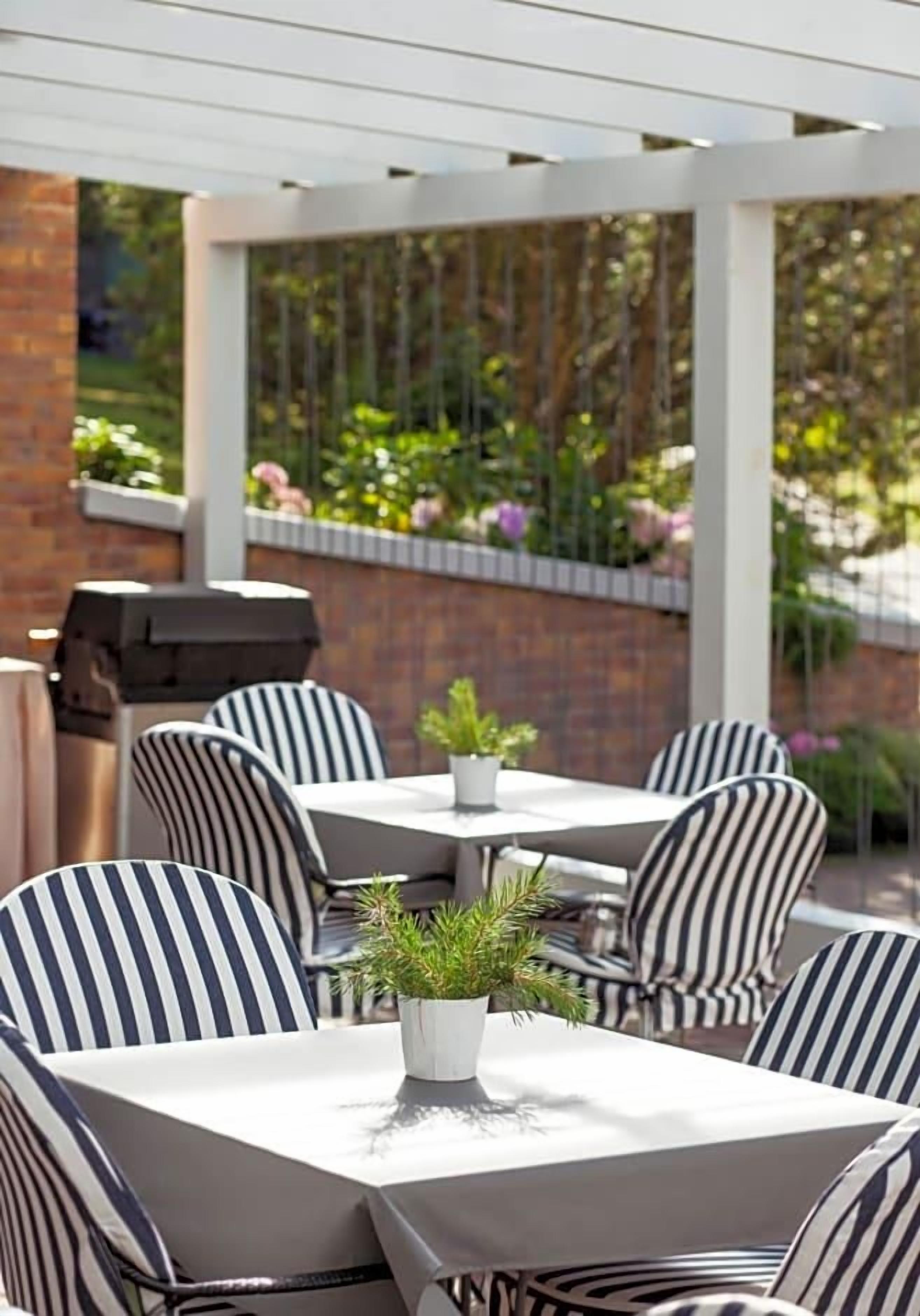 An outdoor patio area with striped chairs and tables, a grill, and potted plants.