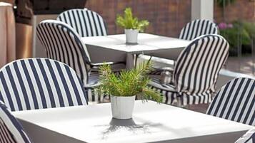 Un patio al aire libre con sillas y mesas a rayas, una parrilla y plantas en macetas.