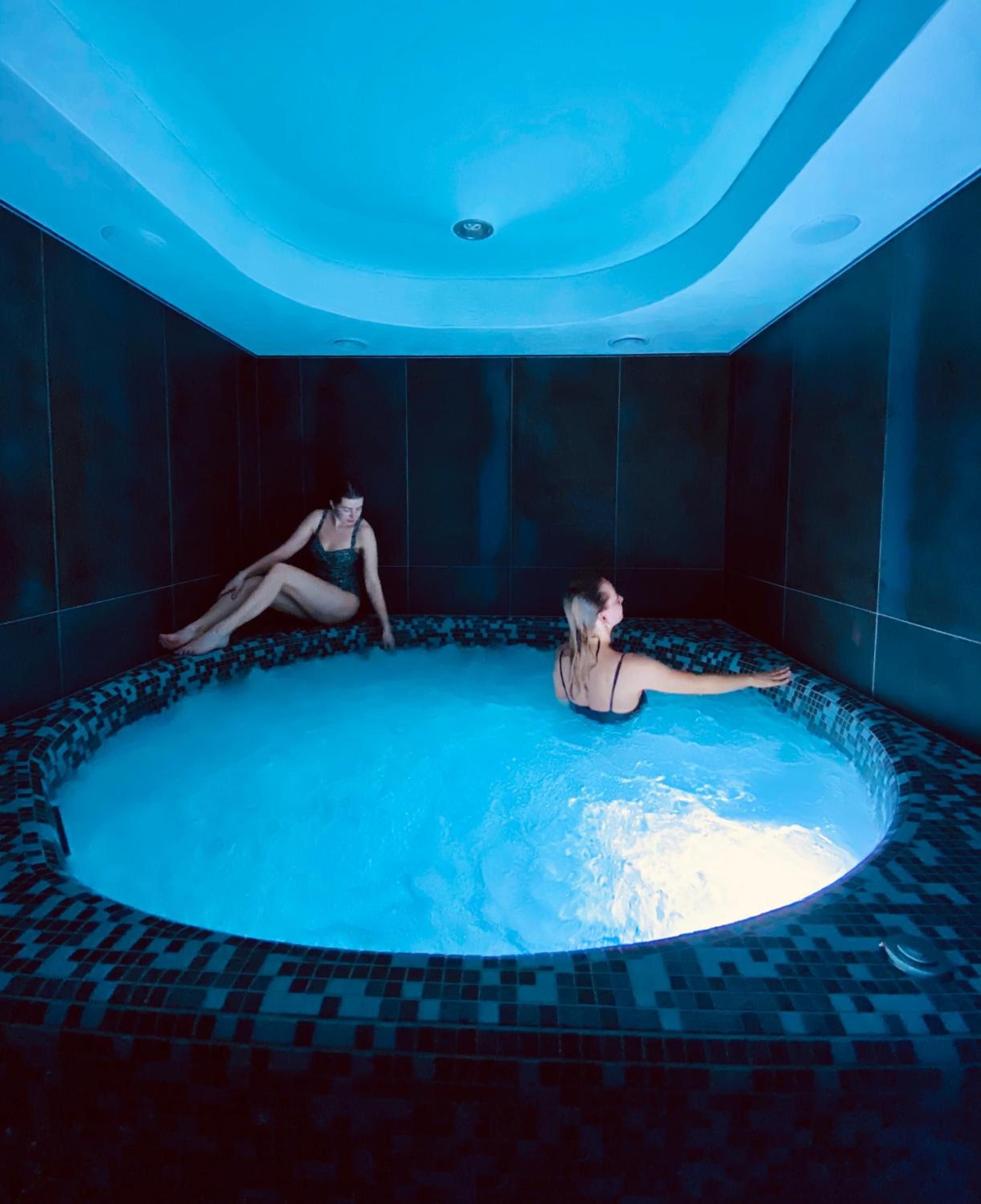 Una amplia piscina interior con suelo y paredes de azulejos, rodeada de baldosas oscuras.